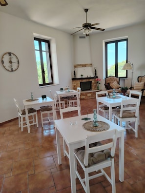 Un espace repas avec des tables et des chaises blanches, une cheminée et un ventilateur de plafond.