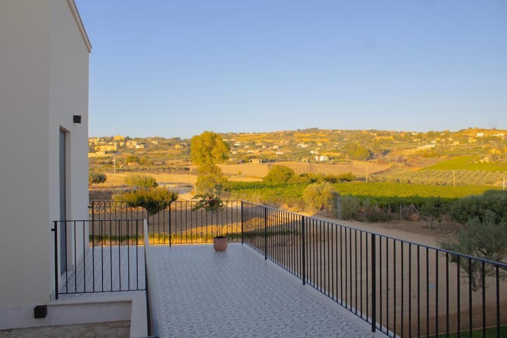 A balcony with a view of a vineyard and distant houses.