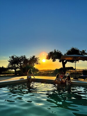 Piscina con vista sul tramonto, circondata da alberi e una zona coperta.