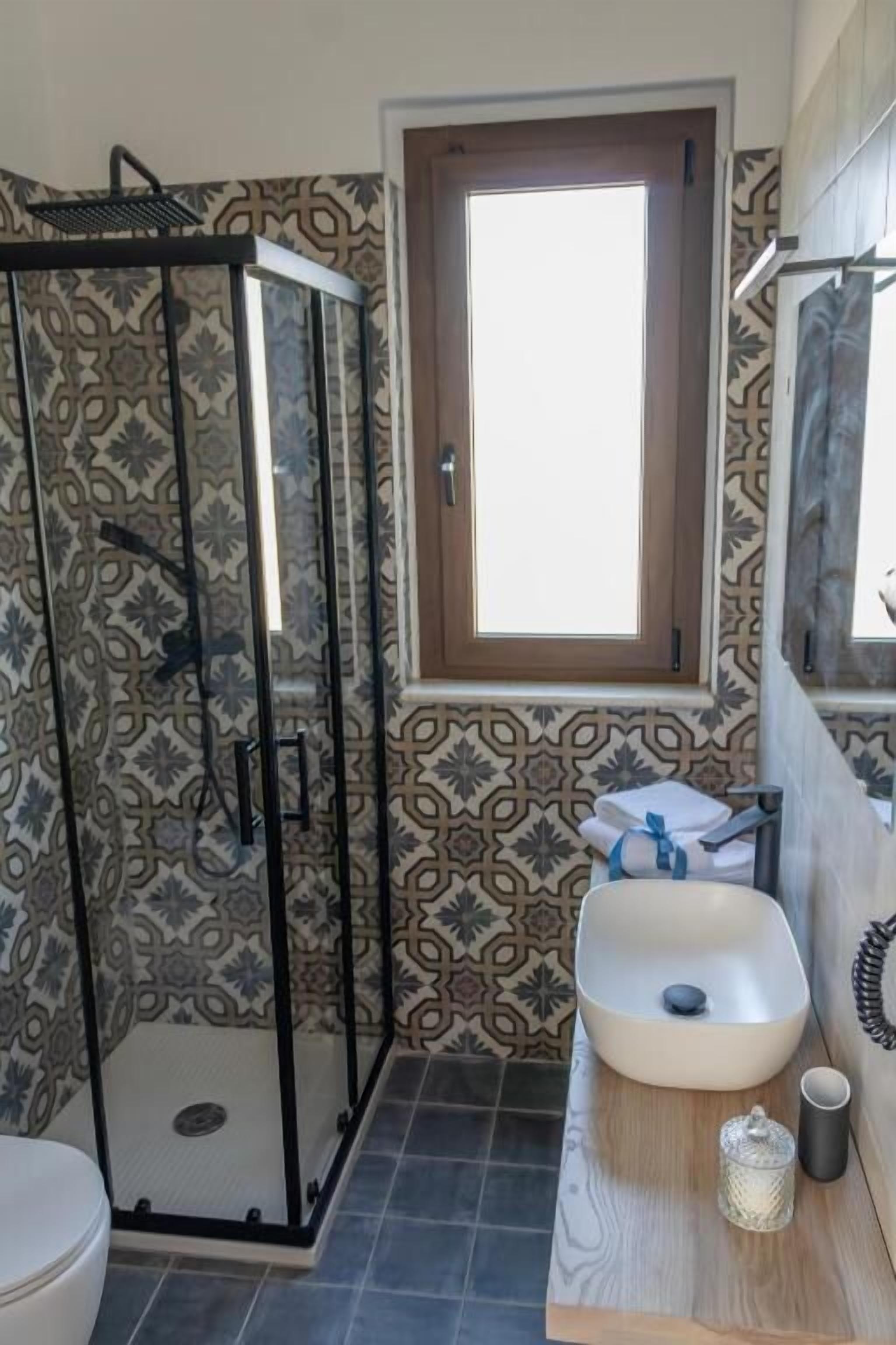 Une salle de bain avec une douche, un lavabo avec un miroir et un papier peint à motifs.