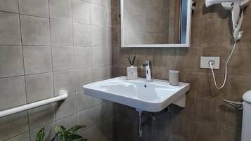 Un baño con lavamanos blanco, espejo, secador de pelo y planta en maceta.