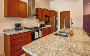 A kitchen with granite countertops, a stove, a refrigerator, and wooden cabinets. - Private Terrace with Views, Pool & Gym Access (Cabo San Lucas)