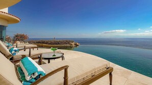 Un área junto a la piscina con sillones de descanso, una mesa y vistas al océano.