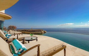 Ein Poolbereich mit Liegestühlen, einem Tisch und Blick aufs Meer.