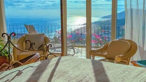 Un balcón con vista al océano, muebles de mimbre y una lámpara colgante.