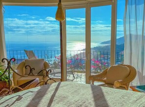 Ein Balkon mit Blick auf das Meer, Korbmöbel und einer hängenden Leuchte.