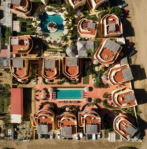 Eine Vogelperspektive zeigt einen Urlaubsort mit mehreren Bungalows, einem zentralen Swimmingpool und umgebender Vegetation.