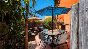 Eine Terrasse im Freien mit Tisch und Stühlen, umgeben von Pflanzen und einem Holzzaun.
