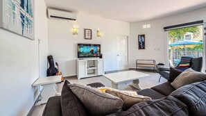 Ein Wohnzimmer mit Fernseher, Gitarre, Sofa und Couchtisch.