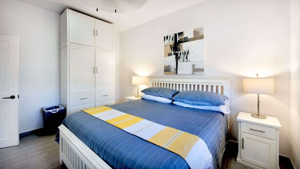 Een slaapkamer met een bed, twee nachtkastjes, een kledingkast en een kunstwerk aan de muur.