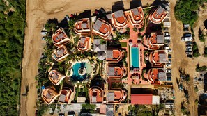 Eine Vogelperspektive auf ein Resort mit mehreren bungalowsartigen Unterkünften, einem zentral gelegenen Swimmingpool und einer Sandstrandanlage.