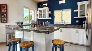 A modern kitchen with a central island, white cabinetry, and a blue accent wall. - Ground Floor Condo with Pool, Near Cerritos Beach (El Pescadero)