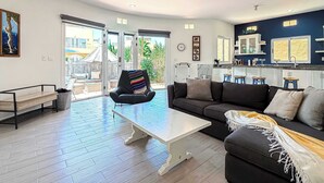 Een moderne woonkamer met een bank, een salontafel en een stoel. Er is een balkon met uitzicht op gebouwen en bomen.