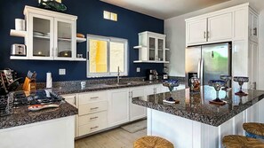 A modern kitchen with white cabinetry, granite countertops, and a built-in island with stools. - Ground Floor Condo with Pool, Near Cerritos Beach (El Pescadero)