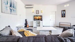 A living room with a sofa, a TV, a guitar, and a door. - Ground Floor Condo with Pool, Near Cerritos Beach (El Pescadero)