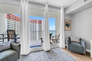 Ein Balkon mit Blick auf ein Hochhaus, ein Sessel, eine Couch und ein Teppich.