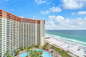 Ein Hochhotel mit mehreren Balkonen, einem Poolbereich und Blick auf den Strand.