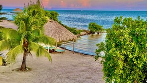 Una spiaggia con una capanna a tetto di paglia, palme e vista sul mare.