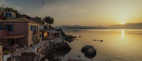 A coastal property with a stone building, outdoor seating, and a dock extending into calm waters.