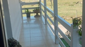 Un balcón cubierto con vistas a un paisaje rural, plantas en macetas y un tapete decorativo.