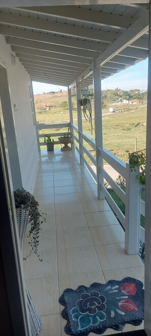 Ein ĂŒberdachter Balkon mit Blick auf eine lĂ€ndliche Landschaft, mit Topfpflanzen und einem dekorativen Teppich.
