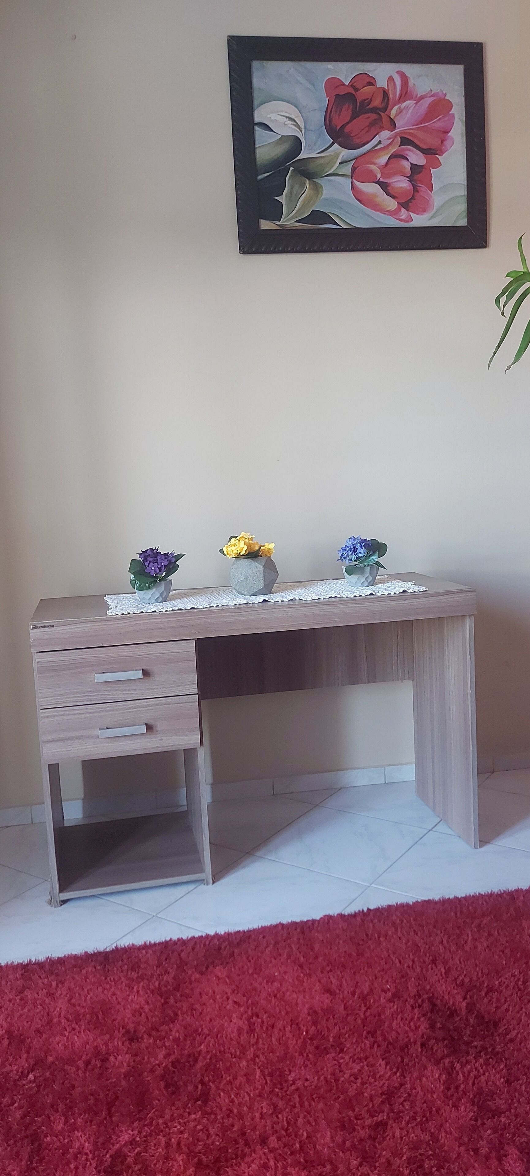 A desk with drawers, a lace tablecloth, and three vases with flowers.