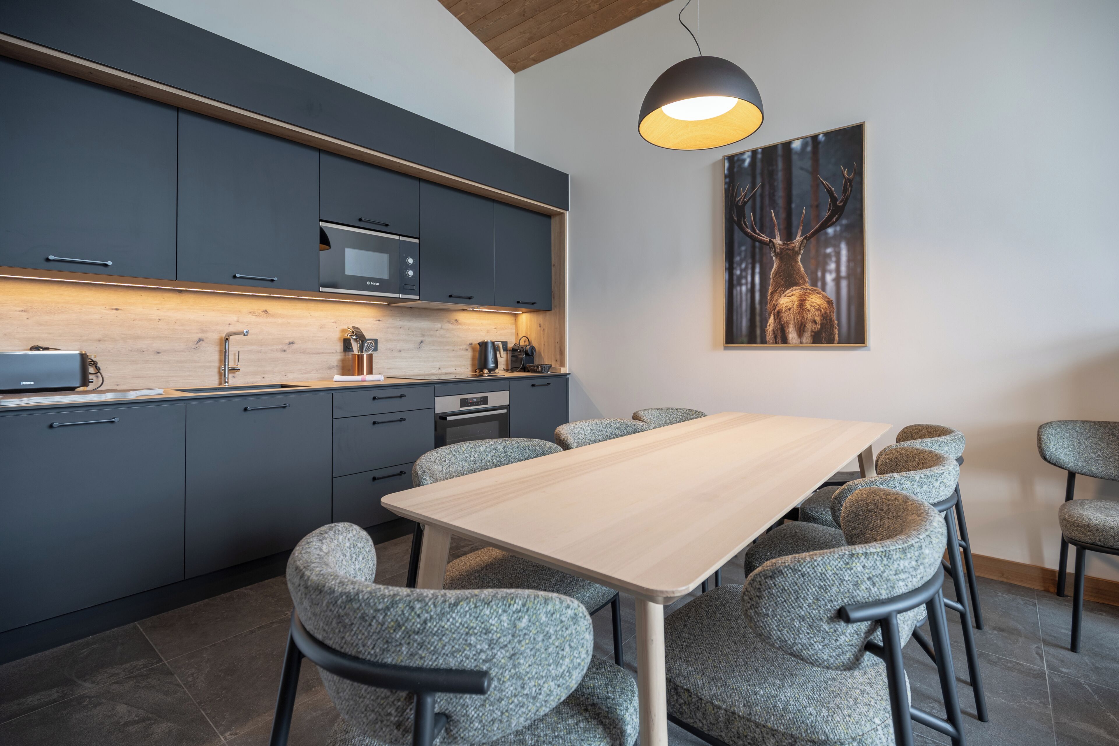 Une cuisine moderne avec des meubles de couleur sombre, un plan de travail en bois et un coin repas comprenant une table et des chaises.