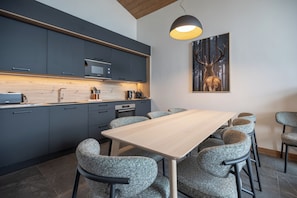 A modern kitchen with dark cabinets, a wooden countertop, and a dining area with a table and chairs. - TERRESENS - Les Balcons de Juliette (Notre-Dame-de-Bellecombe)