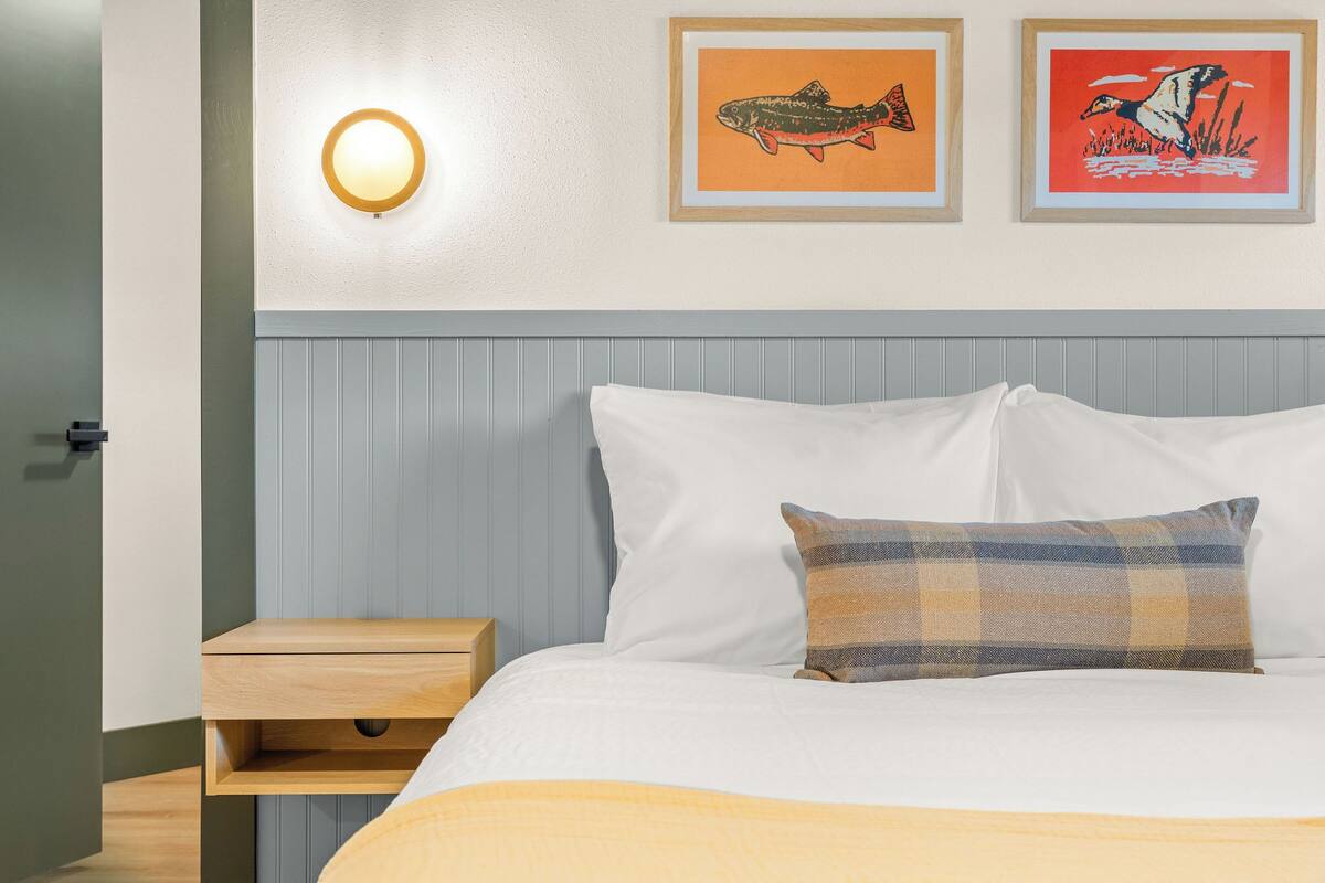 A neatly made bed with white and plaid pillows, a bedside table, and two framed pictures on the wall.