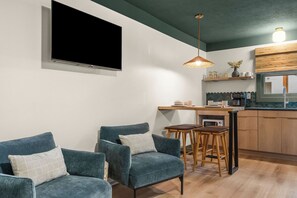 A modern living room with a flat-screen TV, two sofas, a coffee table, and a kitchen area with wooden cabinets and a window. - The Drift Resort (Branson)
