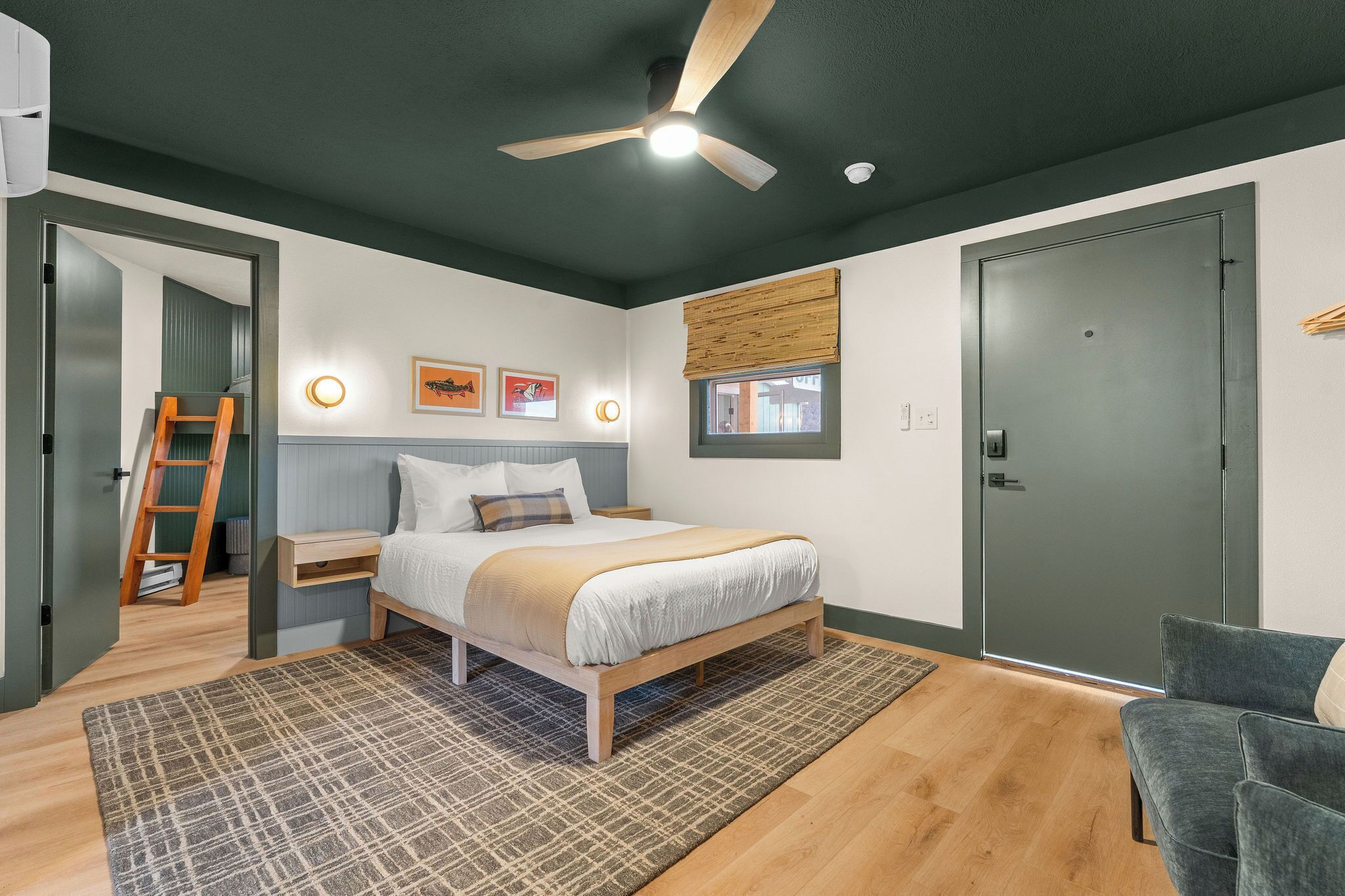 A bedroom with a bed, bedside tables, a ceiling fan, a window with blinds, and a door.