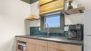 A kitchen with a window, a sink, a microwave, a coffee maker, and wooden cabinets. - The Drift Resort (Branson)