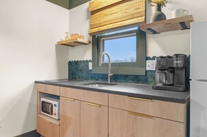 A kitchen with a window, a sink, a microwave, a coffee maker, and wooden cabinets.