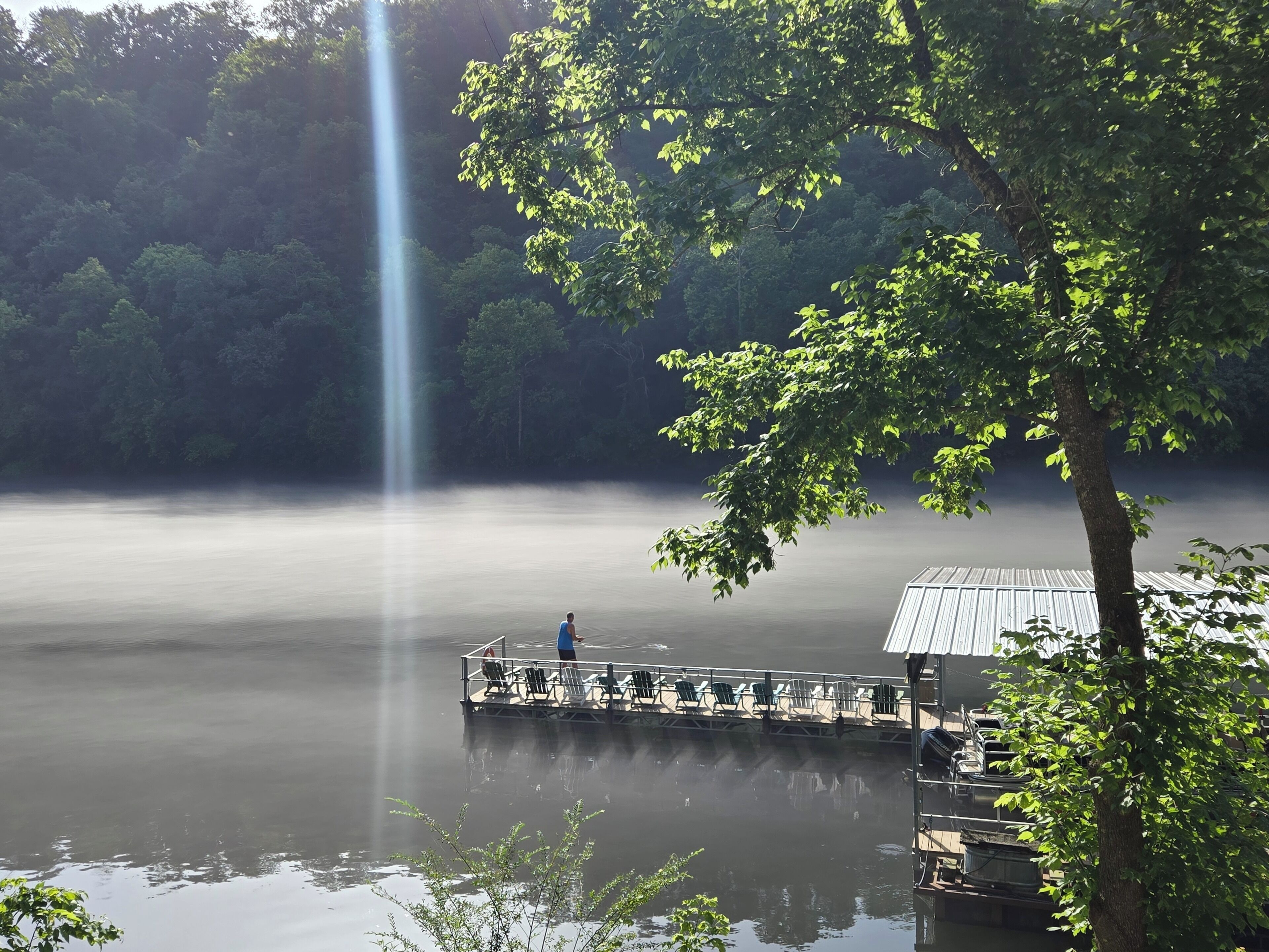 A calm lake with a pier extending into the water, surrounded by trees and a clear sky.