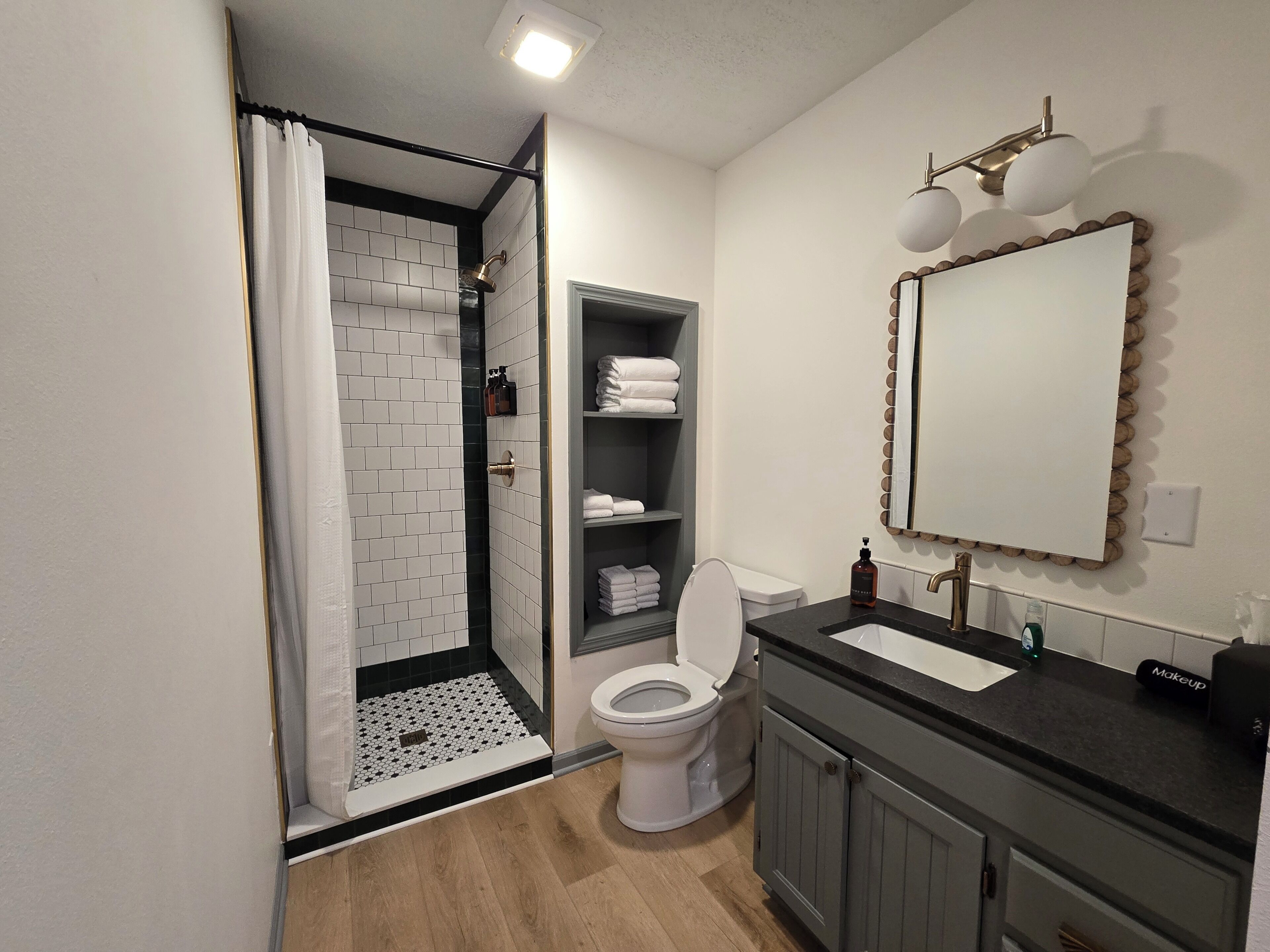 A bathroom with a shower, toilet, sink, and a mirror with a decorative frame.
