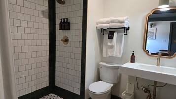 A bathroom with a shower, toilet, sink, and a mirror.
