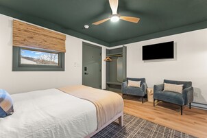 Un dormitorio con cama, dos sillones, ventilador de techo, televisión y ventana con persianas.