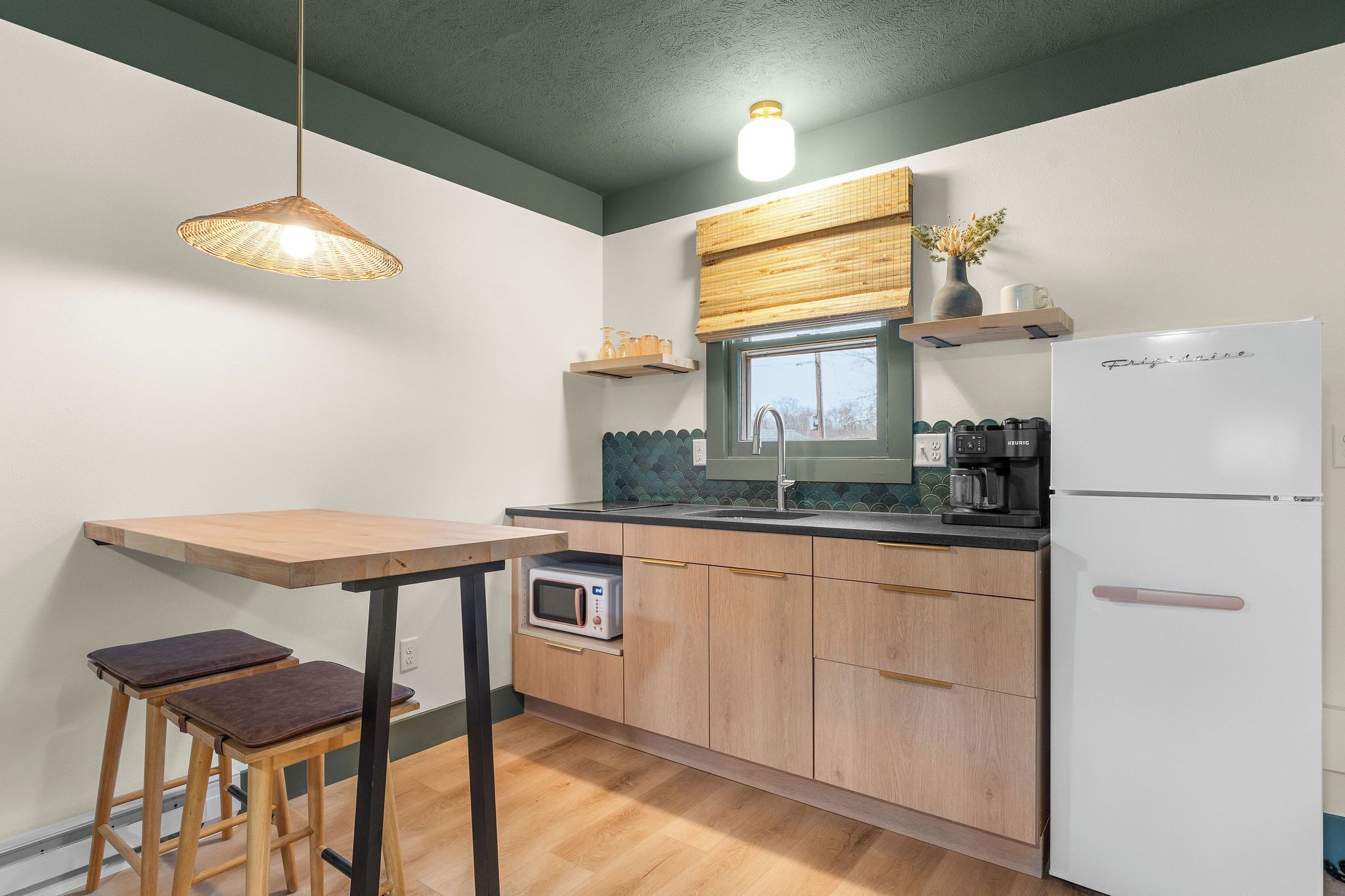 A kitchen with a wooden table, stools, a microwave, a refrigerator, and a hanging light fixture.