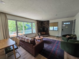 A living room with a stone fireplace, a television, a dining table, and a green armchair.