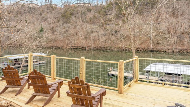 A deck with wooden chairs overlooking a calm body of water, a dock, and a hilly landscape in the background. - The Drift Resort (Branson)