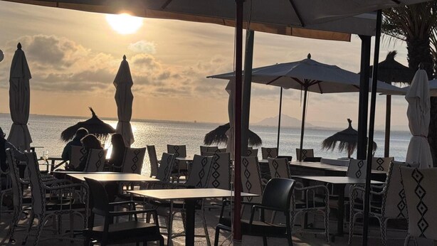 An outdoor seating area with tables and chairs, umbrellas, and a view of the sea.