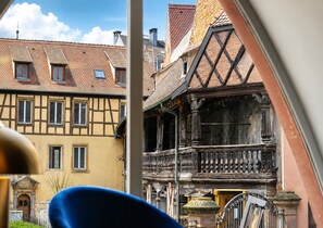 Un bâtiment traditionnel à colombages, doté d’un balcon, avec un ciel dégagé et, au loin, on aperçoit un bâtiment moderne.