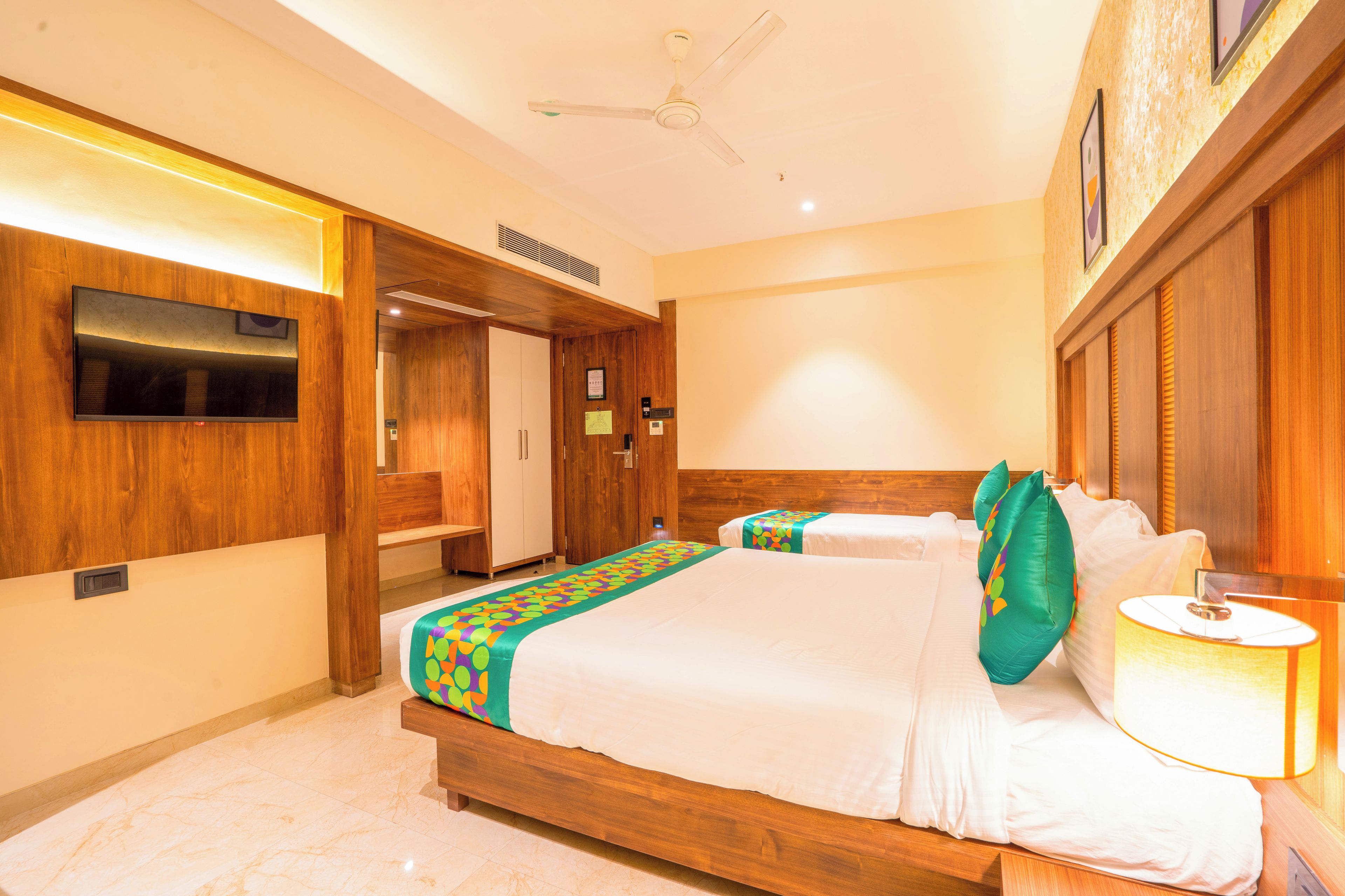 A hotel room with a bed, bedside table, lamp, wardrobe, and a ceiling fan.