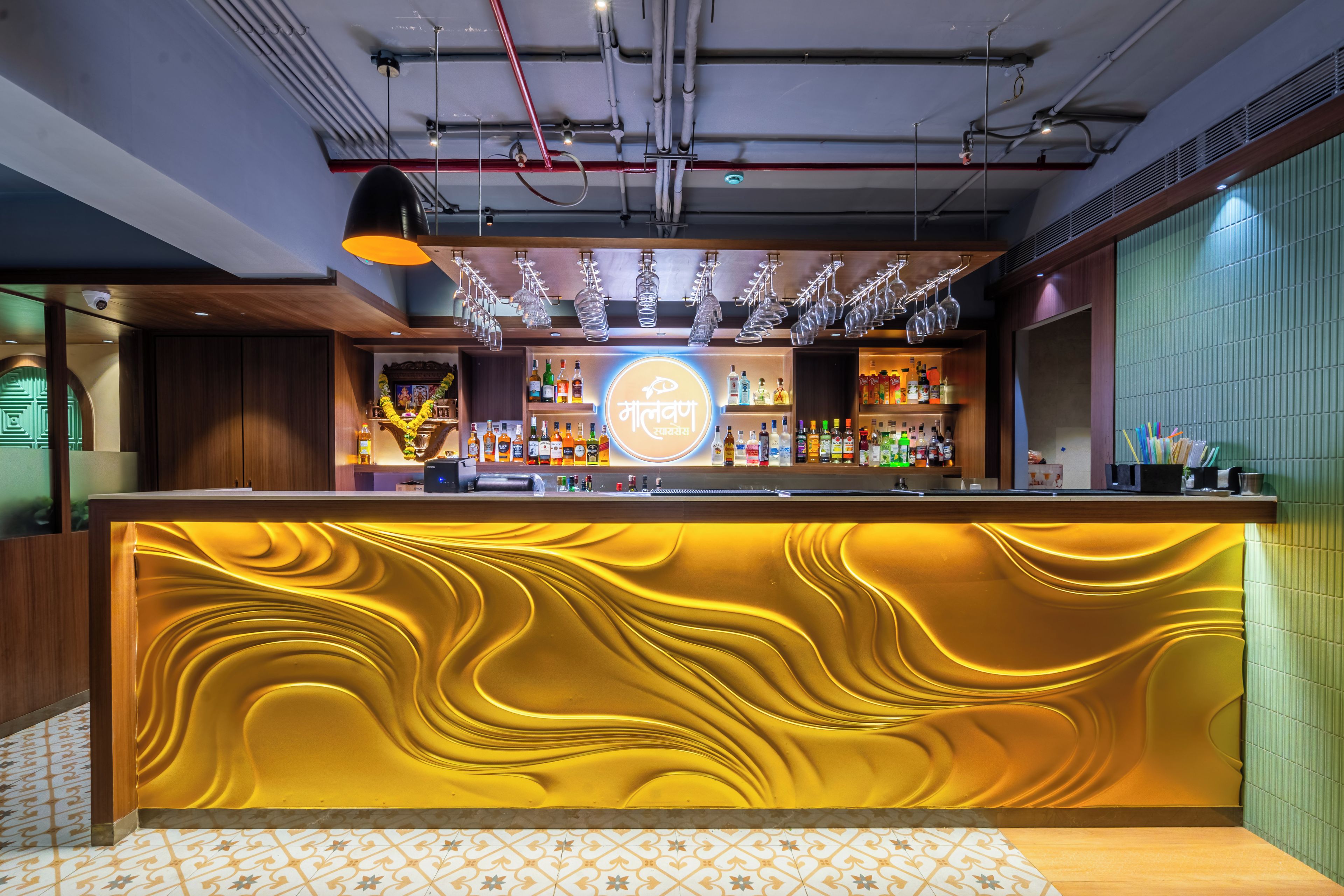 A bar area with a central counter, overhead lighting, and a variety of bottles.