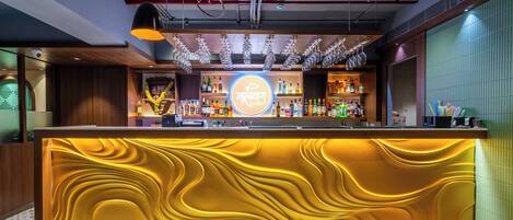 Zona de bar con mostrador central, iluminación colgante y una variedad de botellas.