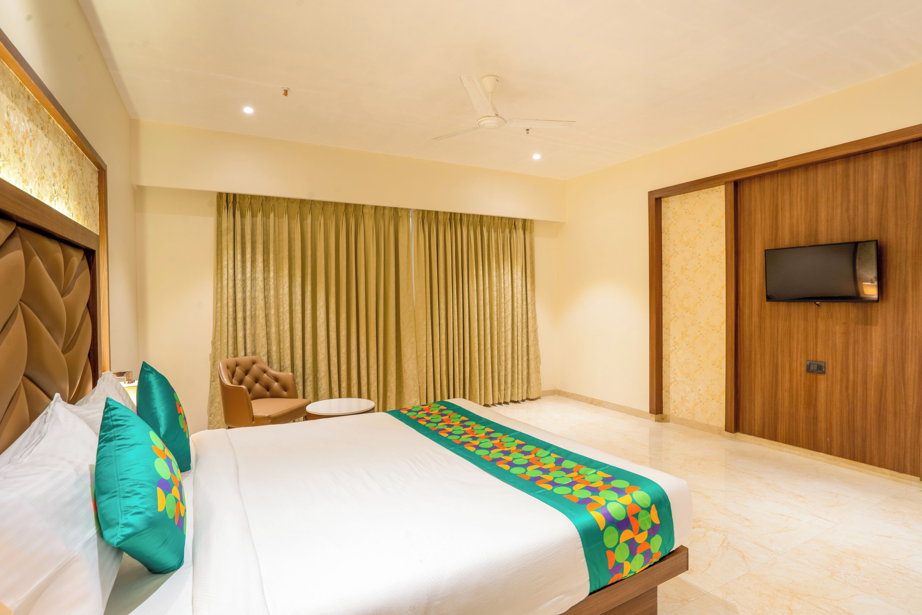 A hotel room with a bed, a chair, a small table, a television, and a curtain.