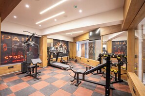 Une salle de sport équipée de matériel d’exercice, dotée d’un mur recouvert de miroirs et ornée d’affiches motivantes.