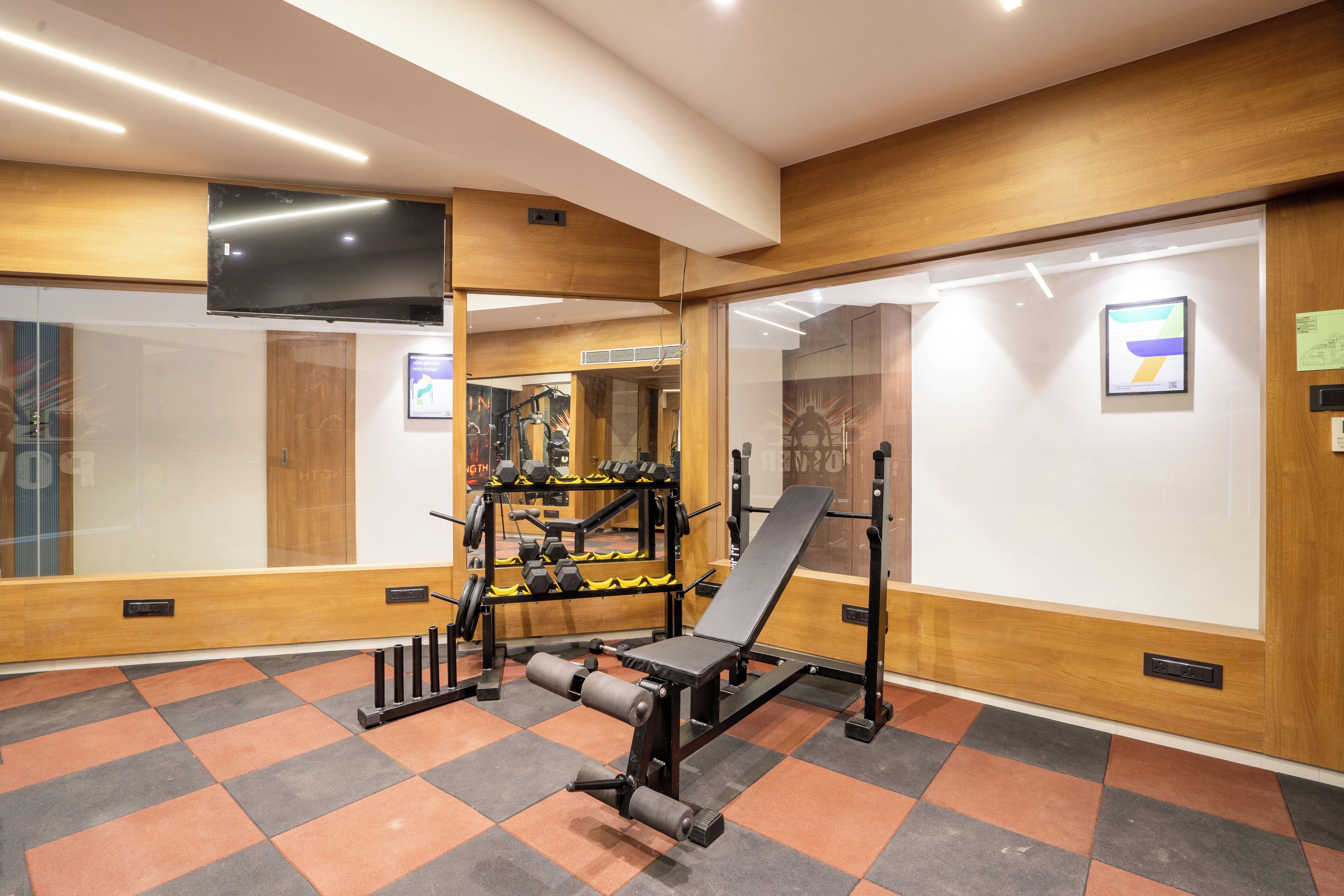 Un gimnasio con equipo de ejercicio, un televisor y un piso estampado.