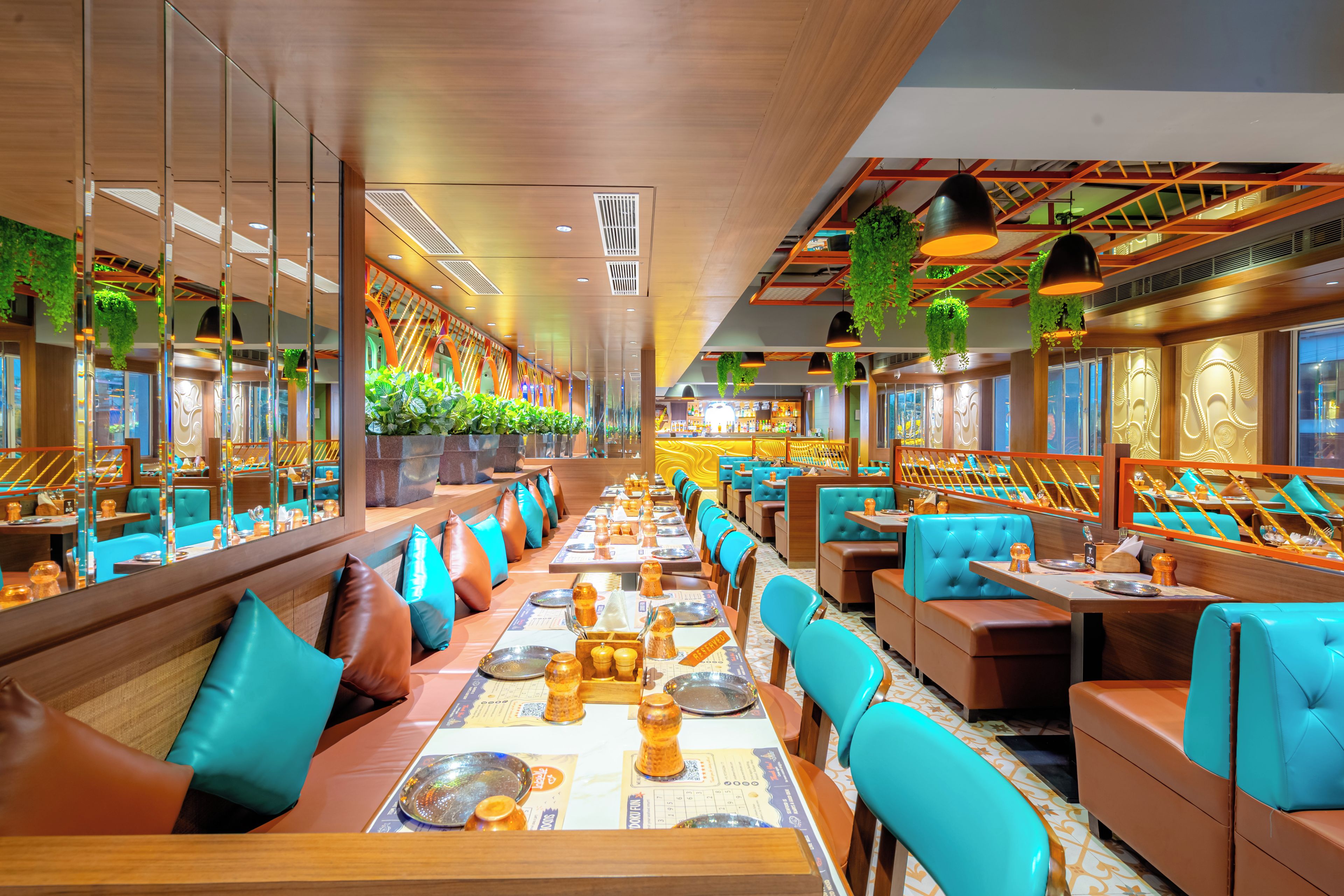 A restaurant with long communal tables, individual booths, and hanging plants.