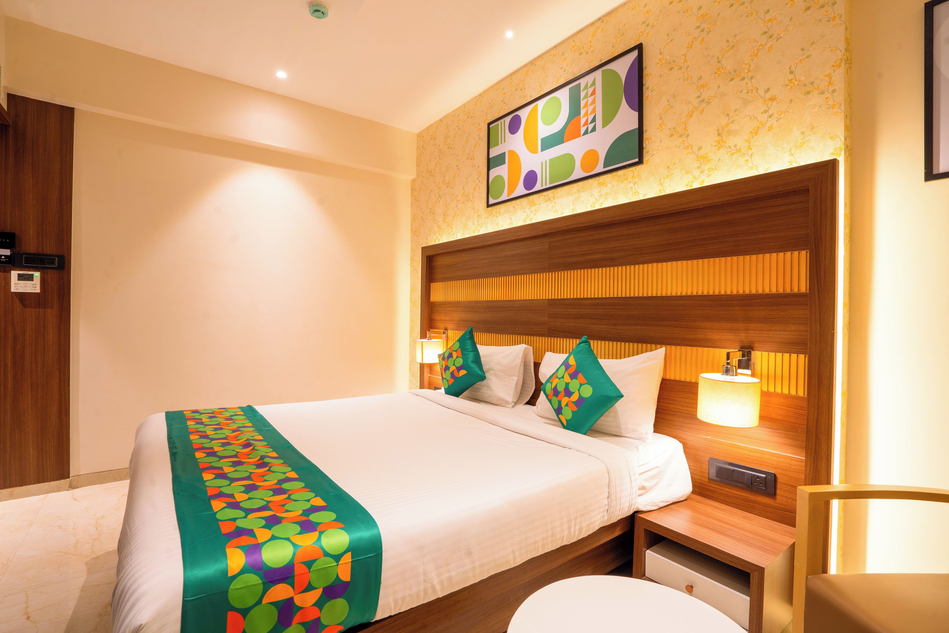 Una habitación de hotel con una cama, una mesita de noche, una lámpara y una obra de arte colgada en la pared.
